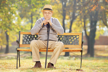 Thoughtful senior man with a cane sitting on bench in a park