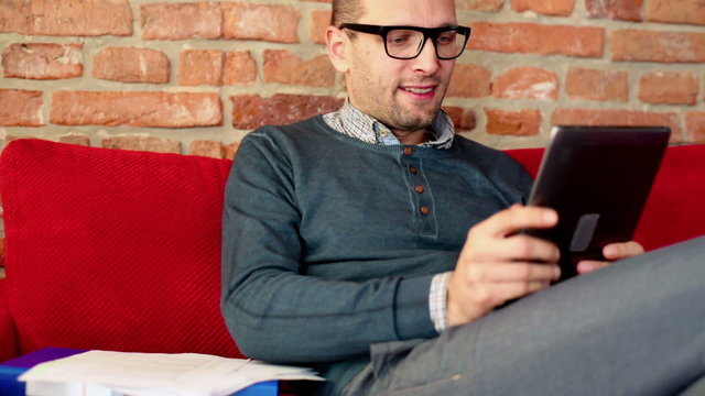 Man using a tablet and sitting on the sofa in his flat