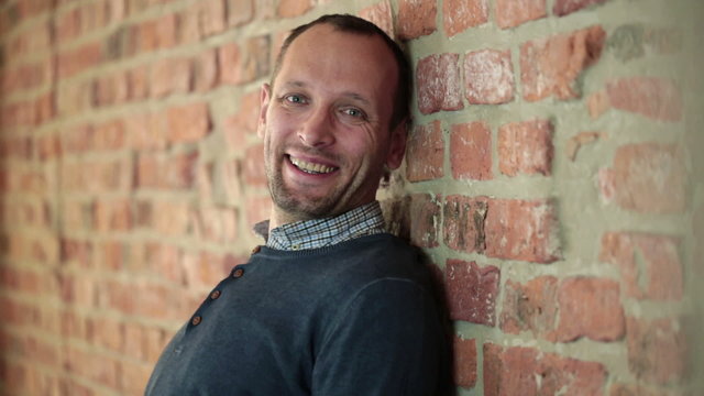 man standing by the brick wall and smiling to the camera