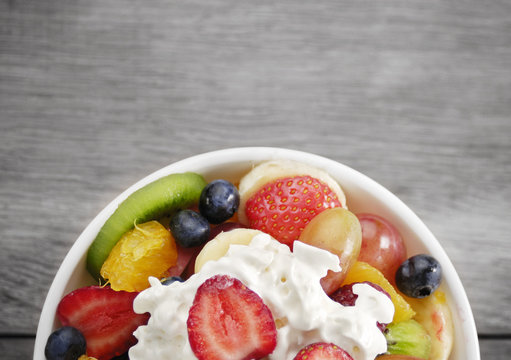 Sweet tasty fruit salad in the bowl with whipped cream