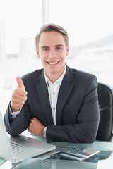 Businessman with laptop gesturing thumbs up at office desk