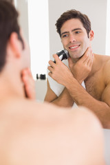 Reflection of shirtless man shaving with electric razor