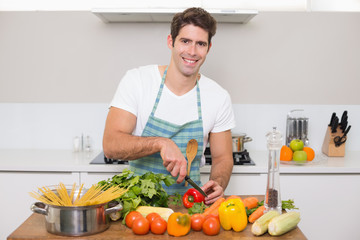 Smiling young man chopping vegetables in kitchen