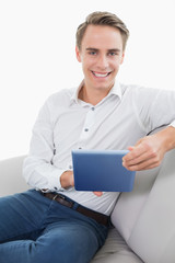 Casual smiling young man using digital tablet on sofa