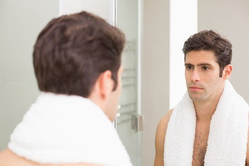 Fototapeta premium Tensed young man looking at self in bathroom mirror