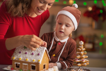 Mother and baby decorating christmas cookie house in kitchen