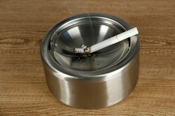 Metal ashtray and cigarette on wooden table