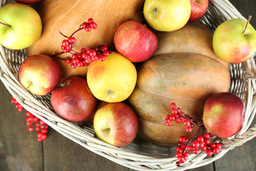Juicy apples and pumpkin in wooden basket on table close-up