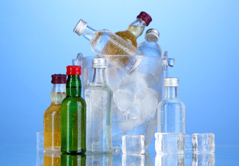 Minibar bottles in bucket with ice cubes,  on color background