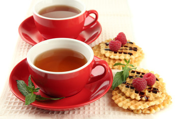 Cups of tea with cookies and raspberries isolated on white