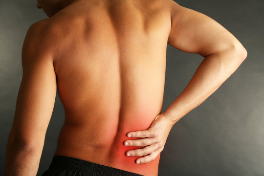 Young man with back pain on grey background