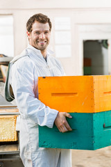 Happy Male Beekeeper Carrying Stack Of Honeycomb Crates