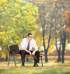 Disappointed young businessman sitting on a bench with bottle