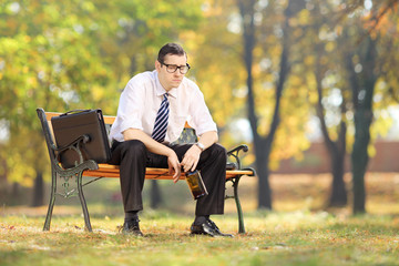 Disappointed young businessperson sitting on a bench with bottle