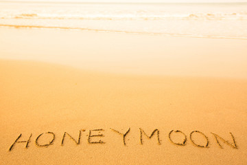 Honeymoon, text written in sand on a beach, with a soft wave.
