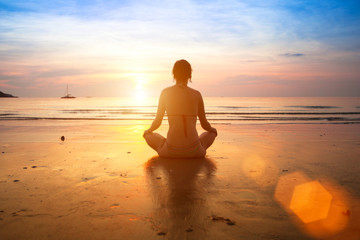 Woman practicing yoga on the beach at sunset.