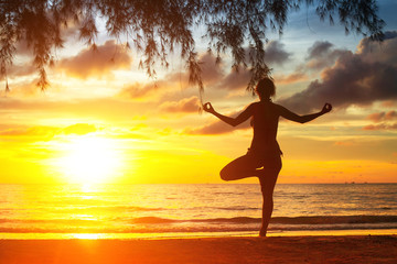 Silhouette of young woman practicing yoga on the sea beach