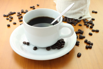 Cup of coffee and part bag beans on wooden table.