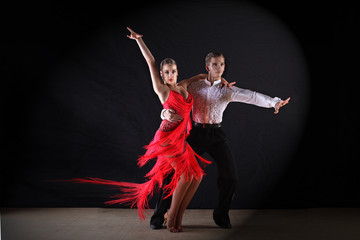 Latino dancers in ballroom against black background