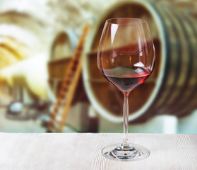 Glass of wine and wooden barrels in winery