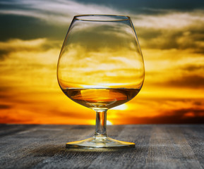 Fototapeta na wymiar Glass of brandy on evening sky background