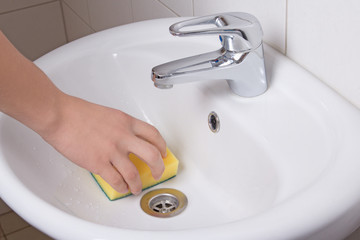 Male hand with yellow sponge cleaning sink