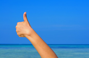 Hand with thumb up on blue sky and sea background