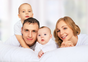 happy family of father, mother and children in white bed