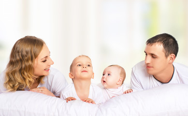 happy family of father, mother and children in white bed