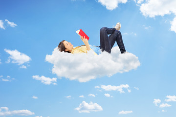 Relaxed female reading a novel and lying on clouds - obrazy, fototapety, plakaty