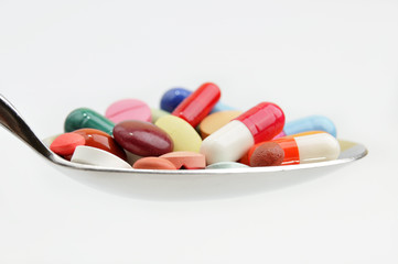 Many different colored tablets and pills on a spoon isolated in