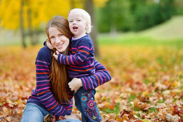 Fototapeta na wymiar Young mother and toddler girl have fun at autumn