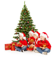 Christmas kids in Santa hat  with presents sitting under fir tre