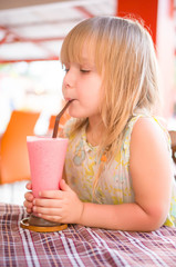 Adorable girl drink pink shake in restaurant