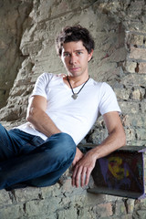 Handsome muscular man sitting near grungy brick wall