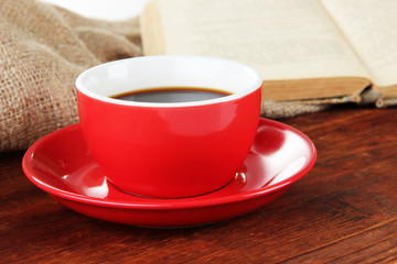 Cup of coffee and book on wooden table on sackcloth background