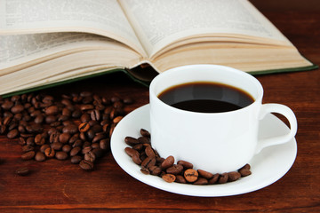 Cup of coffee with coffee beans and book on wooden background