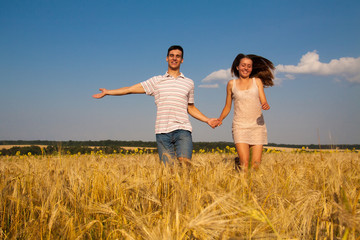 Fototapeta na wymiar Young couple runningthrough wheat field