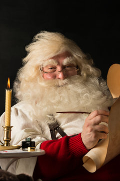 Santa Claus sitting at home and writing on old paper roll to do