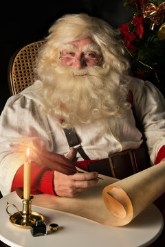 Santa Claus sitting at home and writing on old paper roll to do