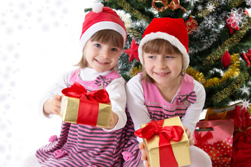 Fototapeta na wymiar Little sisters with gifts under Christmas tree
