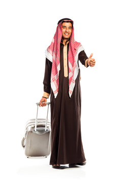Young smiling arab with a suitcase and thumb up isolated on whit