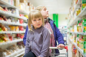 Mother with daughter in shopping cart select products on shelves