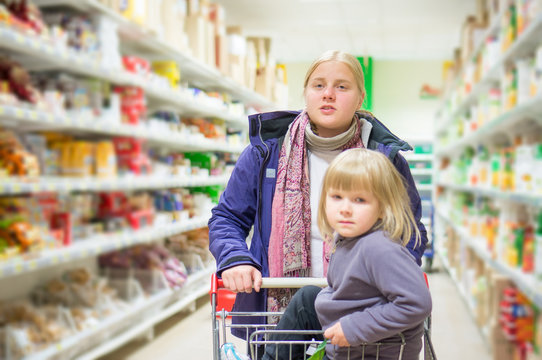 Mother with daughter in shopping cart select products on shelves