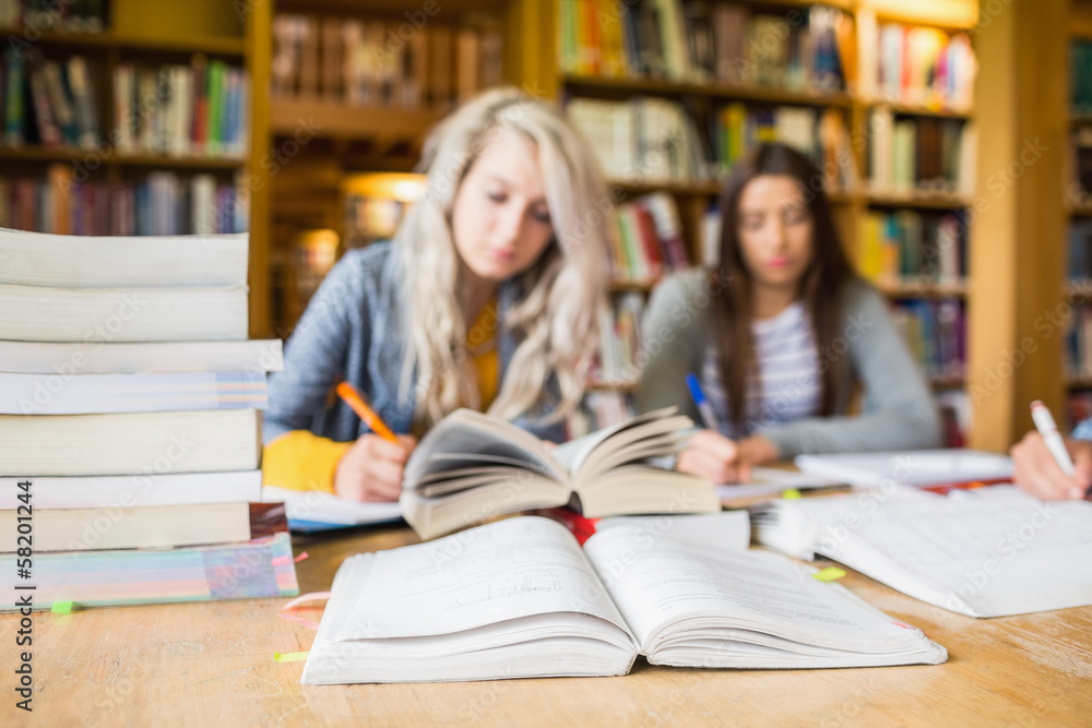 Poster Students writing notes with stack of books at library desk