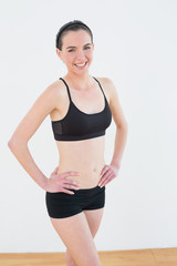 Fototapeta na wymiar Smiling toned woman with hands on hips in fitness studio