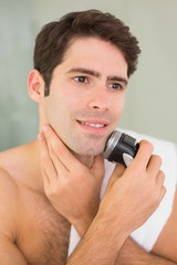 Handsome shirtless man shaving with electric razor