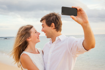 Happy romantic couple on the beach taking photo of themselves wi