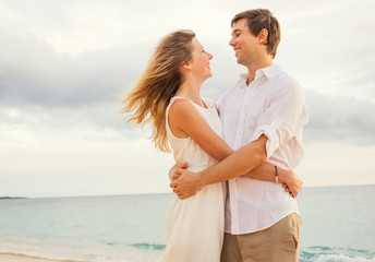 Happy romantic couple on the beach at sunset embracing each othe