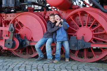 Kinder vor Dampflokrädern umarmen sich freundschaftlich
